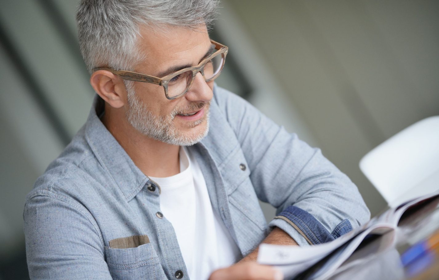 Middle-aged guy with trendy eyeglasses reading magazine