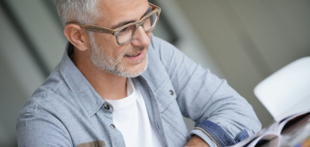 Middle-aged guy with trendy eyeglasses reading magazine