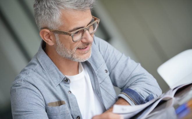 Middle-aged guy with trendy eyeglasses reading magazine
