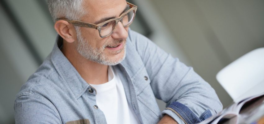 Middle-aged guy with trendy eyeglasses reading magazine