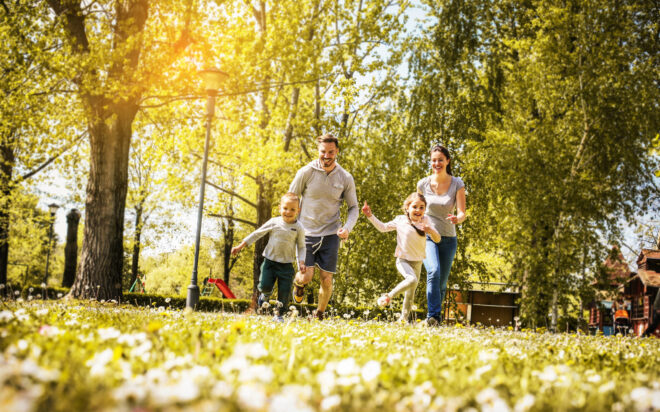 Cheerful family playing with their children's in the meadow. Family having fun in spring day.